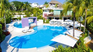 Piscina de un resort con sillones de descanso, palmeras y un edificio con techo de paja.