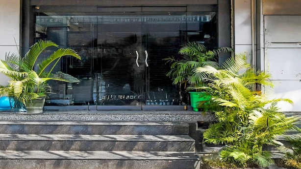 A building entrance with a glass door, steps leading up to it, and potted plants on either side. - Deluxe Hotel Okasu Railway Station (Raipur)