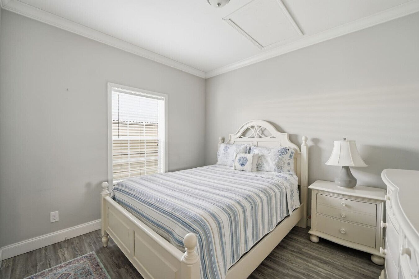 A bedroom with a bed, bedside table, lamp, and a window with blinds.