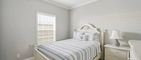 A bedroom with a bed, bedside table, lamp, and a window with blinds.