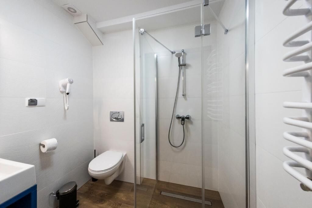 Moderni kylpyhuone, jossa on lasiseinällä varustettu suihku, wc, hiustenkuivaaja ja pyyhekoukku.