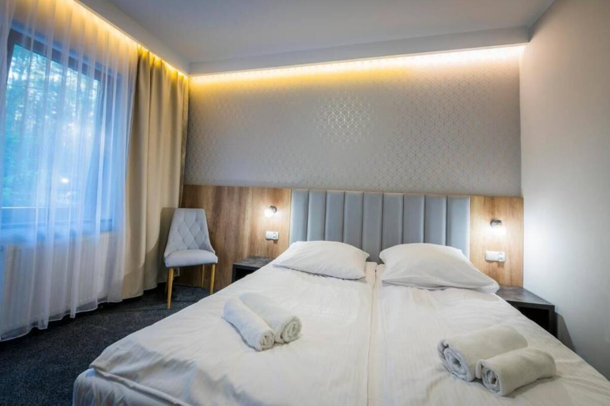 A hotel room with a bed, two bedside tables, a chair, and a window with curtains.