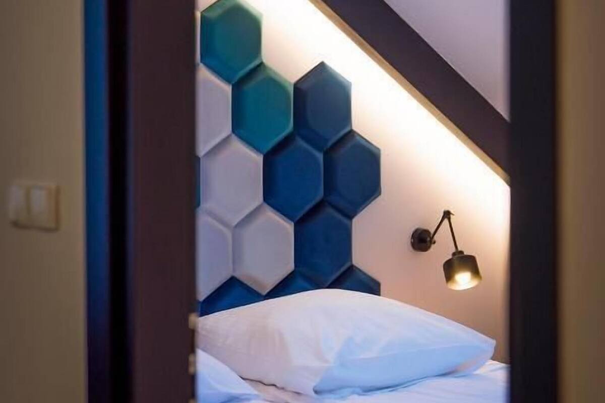 A bedroom with a bed, a wall-mounted light, and a geometric wall design.