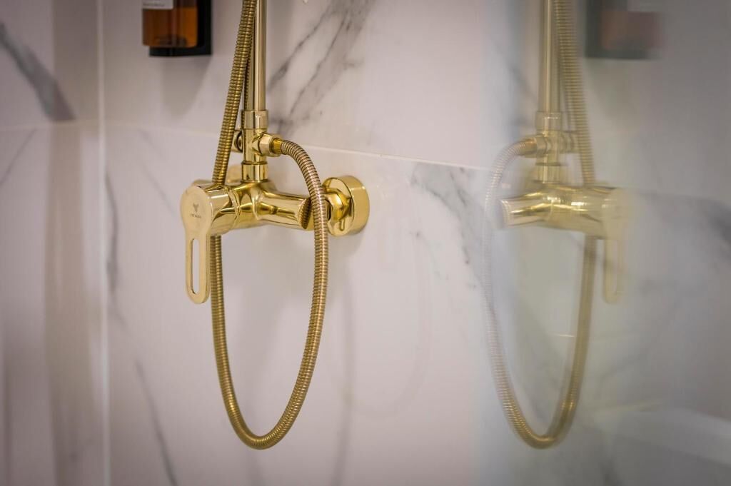 Un cabezal de ducha y manguera dorados frente a una pared de mármol blanco.