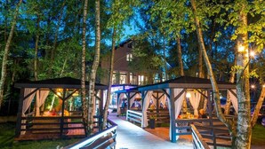 Eine Holzterrasse führt zu einem von Bäumen umgebenen Gebäude bei Nacht.