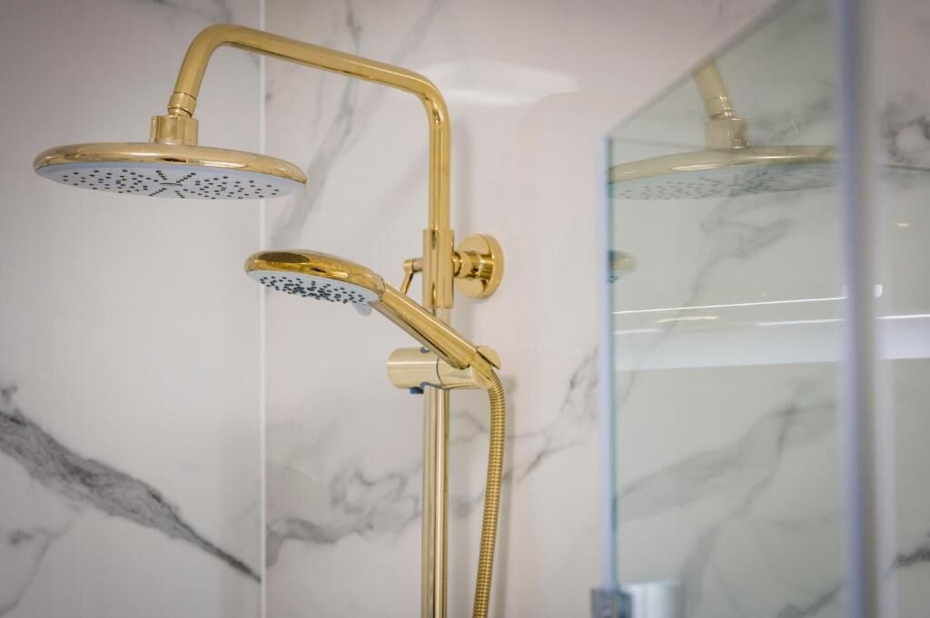Une pomme de douche dorée, un pommeau de douche à main, une pomme de douche murale et un espace de douche en verre.