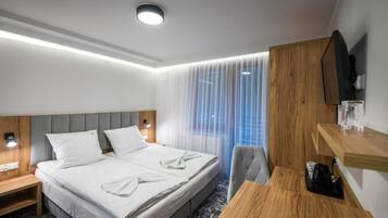 Camera d'albergo con un letto, comodini, una scrivania, una sedia, una televisione e una finestra con tende leggere.
