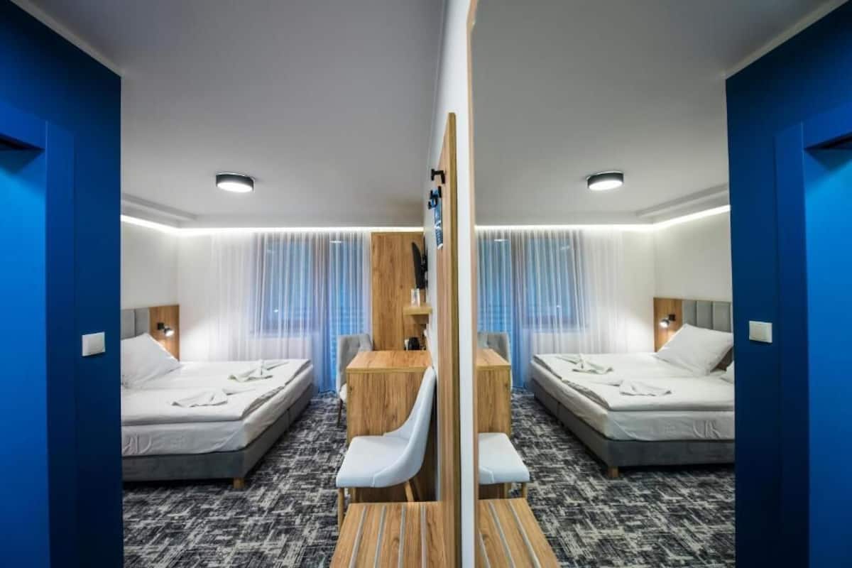 A mirrored room with two beds, a wooden desk, and a chair.