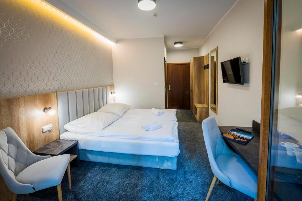 Hotellihuone, jossa on sänky, kaksi tuolia, työpöytä, televisio ja peili.