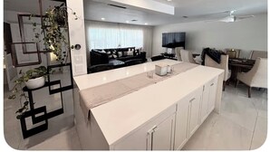 Cozinha moderna com ilha central, eletrodomésticos embutidos e área de refeições com televisão.
