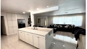 Uma cozinha moderna com armários brancos, uma ilha central e uma área de jantar com sofá e mesa de centro.