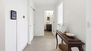 Un pasillo con un banco de madera, una tableta en la pared y una puerta que da al baño.