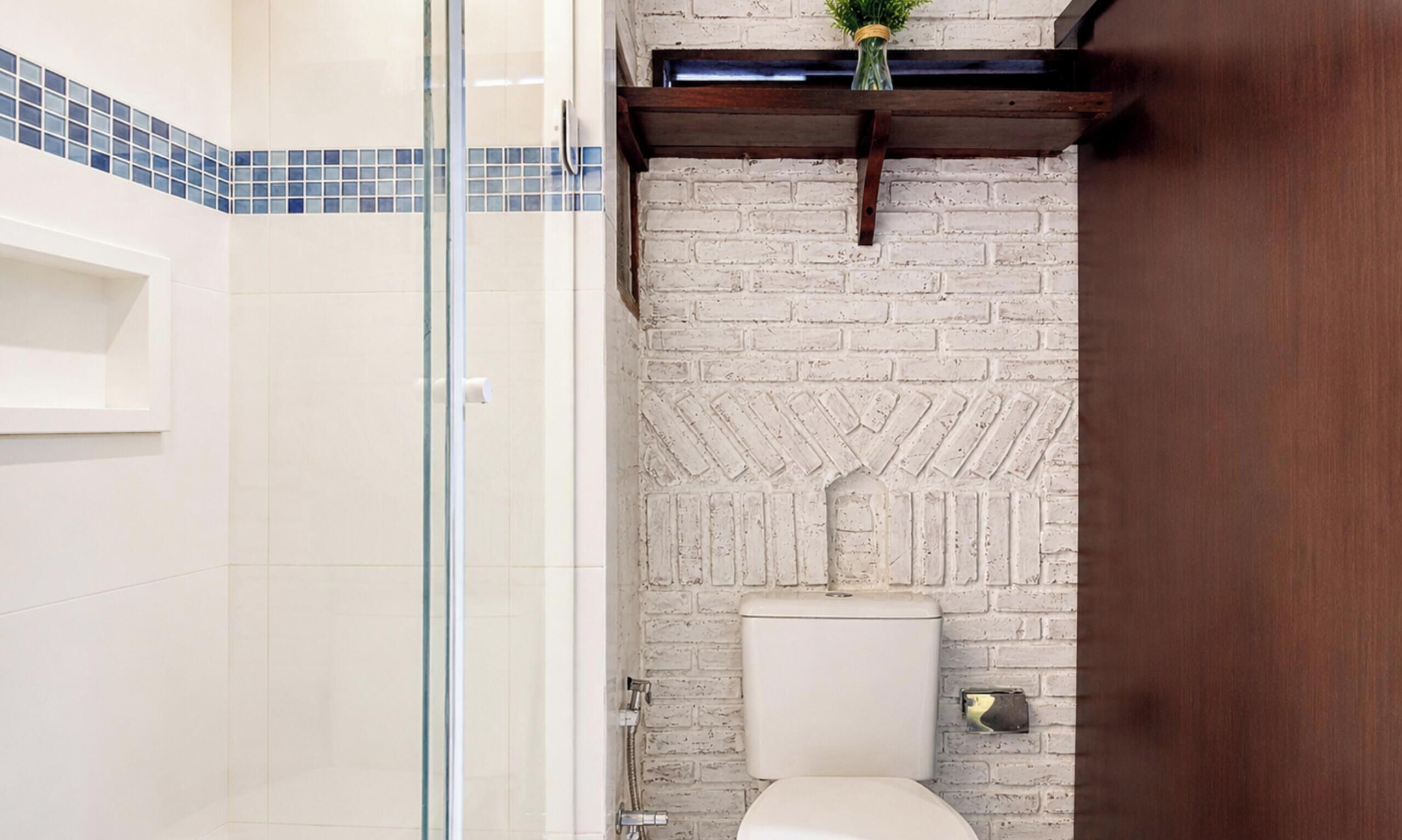 Une salle de bain avec une douche à parois de verre, des toilettes blanches et un mur en briques blanches avec un motif en chevrons.