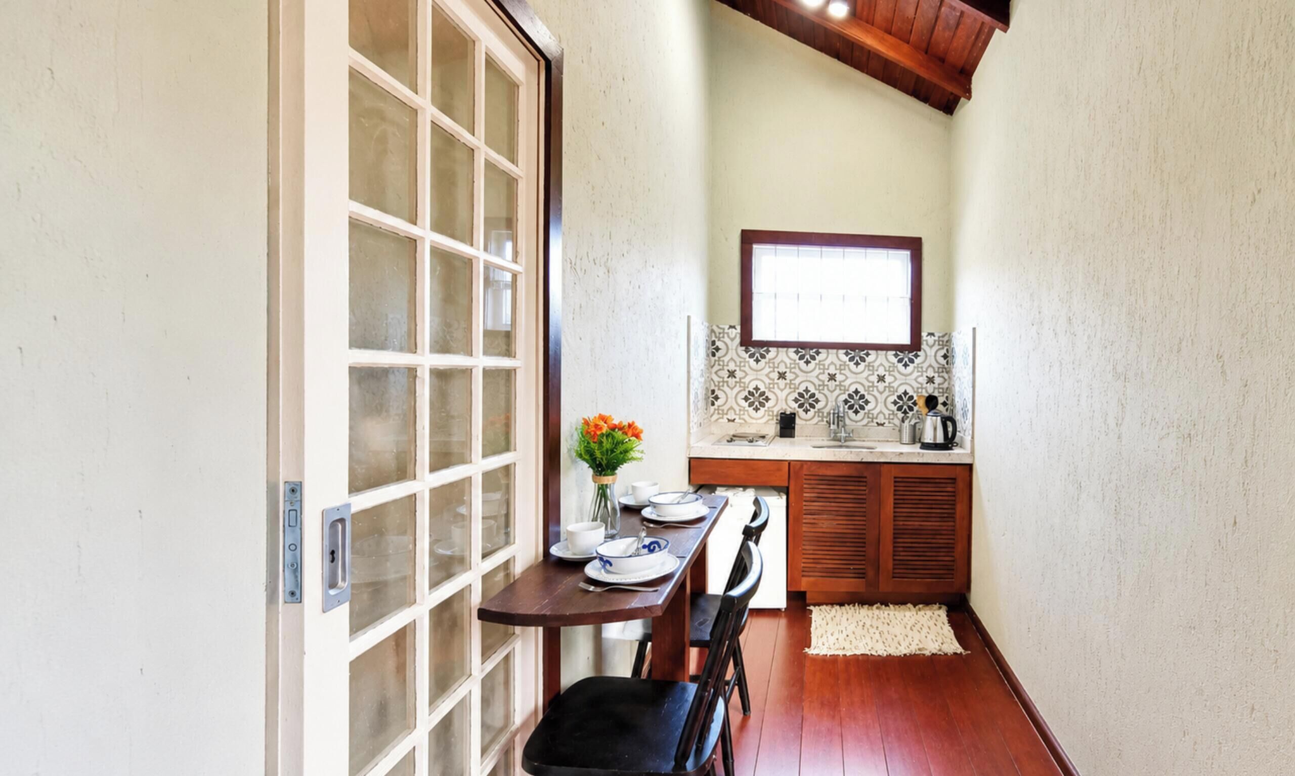 Una cocina estrecha con una mesa para dos personas, una ventana sobre el fregadero y techo de madera.