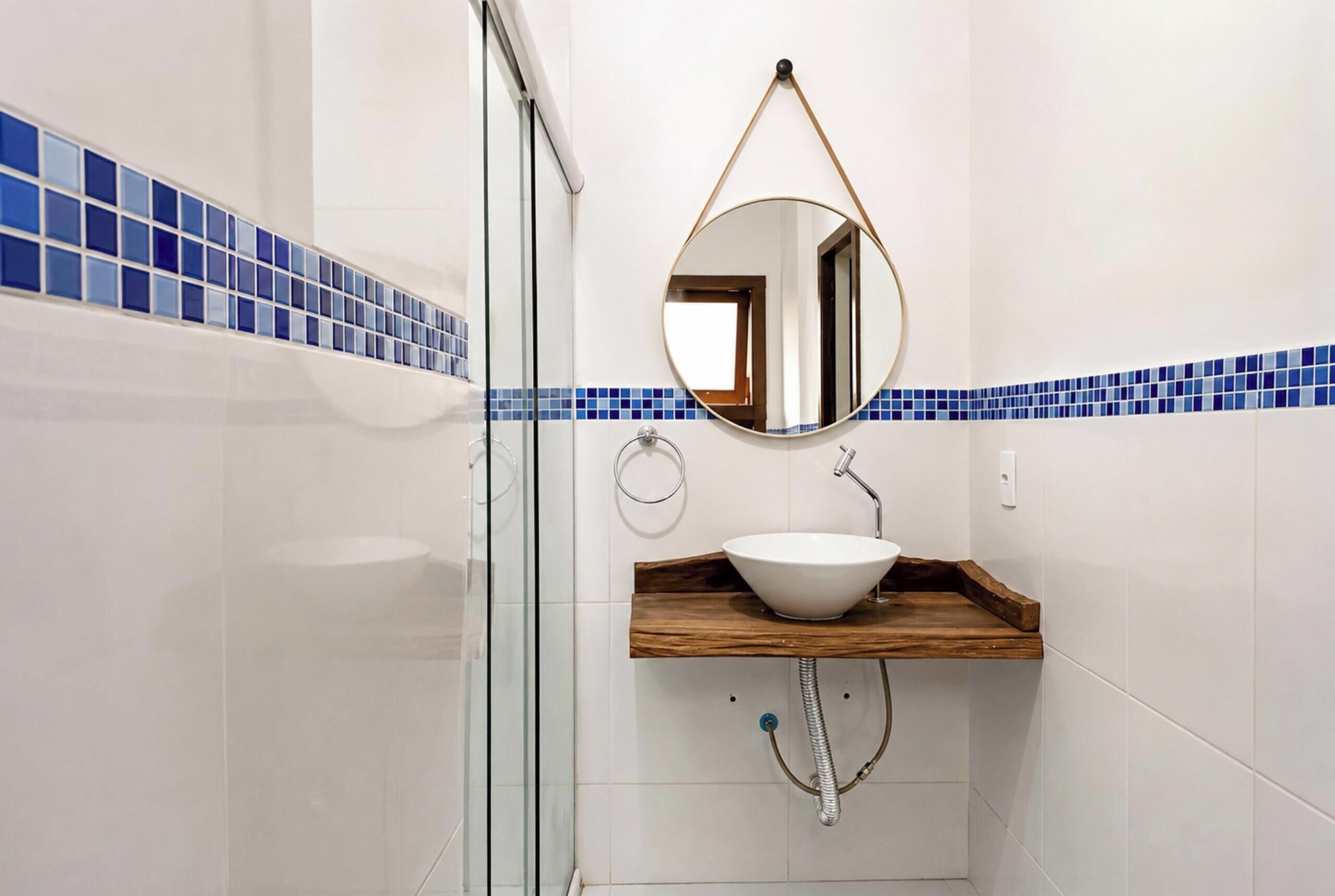A bathroom with a white sink, a wooden vanity, a round mirror, and blue-tiled walls.