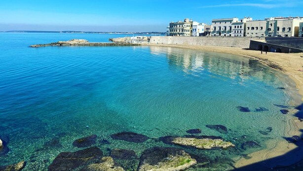 Une ville côtière aux eaux d’un bleu limpide, avec une plage de sable et des bâtiments qui bordent le rivage.