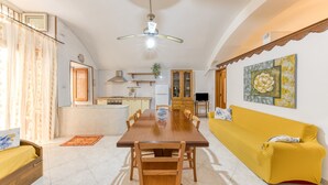 Un vaste espace de vie comprenant une table à manger en bois, un canapé jaune et un ventilateur de plafond.