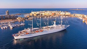 Un grand navire de croisière a accosté dans un port doté d’un port de plaisance, de bâtiments et offrant une vue sur un ciel dégagé.