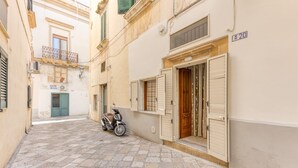 Une rue étroite pavée de pierres, un scooter garé devant un immeuble et une porte avec des volets.