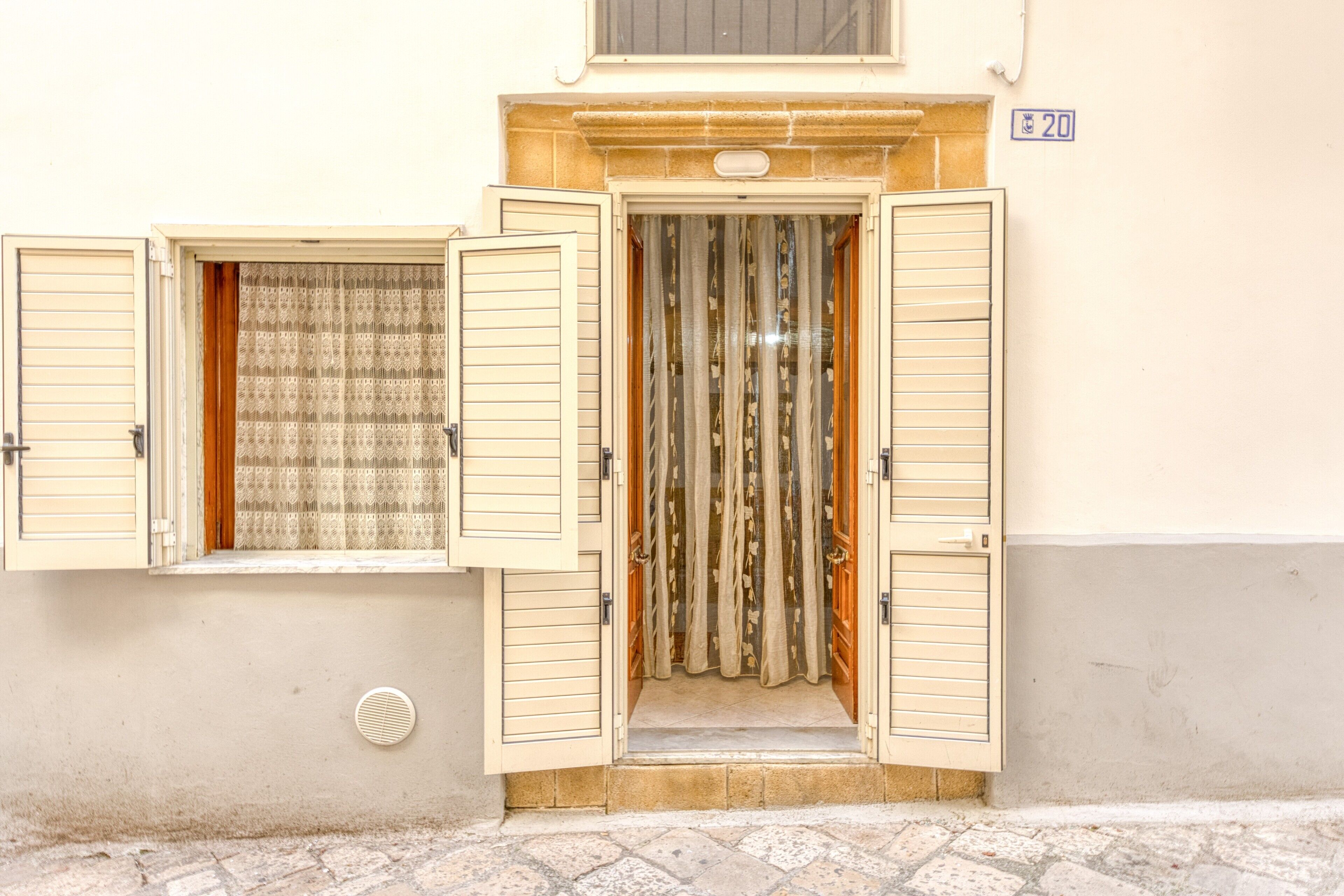 A building entrance with a door, a window with shutters, and a number '20' sign on the wall.