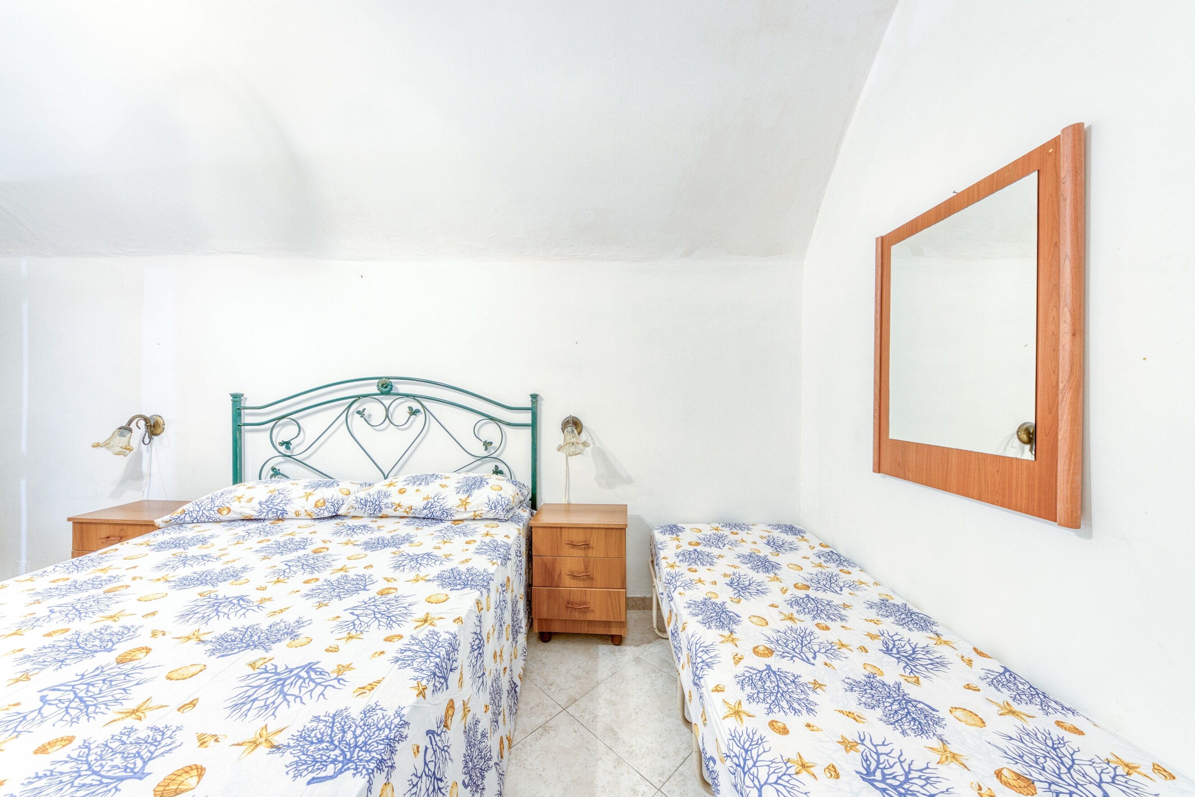 Un dormitorio con dos camas, una mesita de noche de madera, un espejo en la pared y un ventilador de techo.