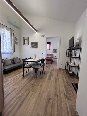 Moderni olohuone, jossa on ruokailutila, sohva, jalustalla oleva televisio ja kirjahylly.
