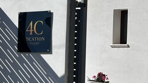 Rakennuksen sisäänkäynti, jossa on kyltti, jossa lukee ”4C LOCATION DELUXE”, pieni ikkuna ja ruukussa oleva kasvi.