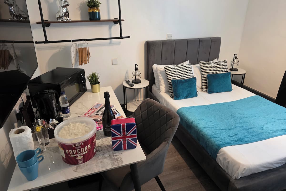 A modern hotel room with a bed, a desk with a computer, a coffee maker, and a small table with snacks.