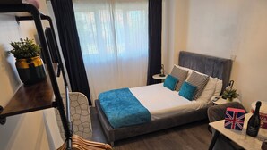 A modern bedroom with a bed, bedside table, lamp, and a small table with a bottle and a box. - Eastwood (Birmingham)