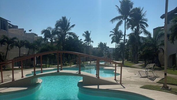 A swimming pool with a bridge, palm trees, and buildings in the background. - Villa Acapulco Diamond (Acapulco de Juárez)