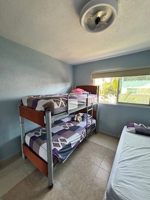 A bunk bed room with a window, a ceiling light, and a bed with a white mattress.