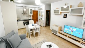 A modern living room with a grey sofa, a dining table with chairs, a TV, and a kitchen in the background. - Holiday apartment in Mogan (Lomo Quiebre)