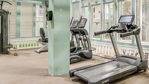 A gym with treadmills and exercise equipment, a covered area with a railing, and a view of a building outside.