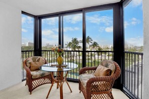 Ein Balkon mit Korbmöbeln, einem Glastisch und einem Blumenstrauß.