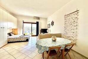 A room with a bed, a sofa, a dining table with chairs, and a wall-mounted decoration. - MONO SUITE - Rena Bianca (Santa Teresa Gallura)
