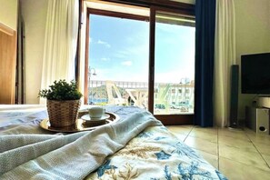 A bedroom with a bed, a potted plant, a tray with a cup, a TV, and a balcony with a view. - MONO SUITE - Rena Bianca (Santa Teresa Gallura)