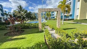 Ein gepflegter Garten mit einem steinernen Torbogen, einem Pool und modernen Gebäuden im Hintergrund.