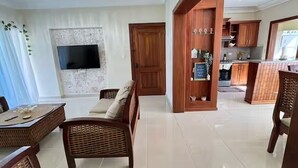 Ein Wohnzimmer mit Fernseher, Korbmöbeln und einer Küchenzeile mit Holzausbau.