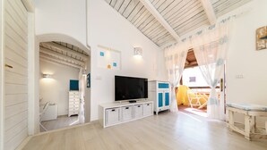 Un salón amplio con televisor, armarios blancos y techo de madera.