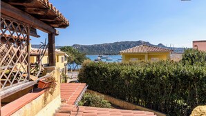 Una propiedad costera con techos de tejas terracota, una pérgola de madera y vistas a barcos en el mar.