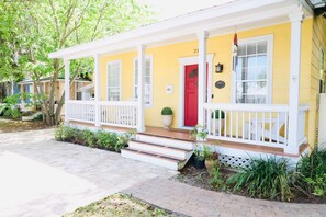 A yellow house with a red door, white porch, and steps leading to the entrance.
