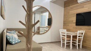 A room with a sofa, a round mirror, a dining table with chairs, and a wall-mounted TV. - Casetta in Calle (Chioggia)