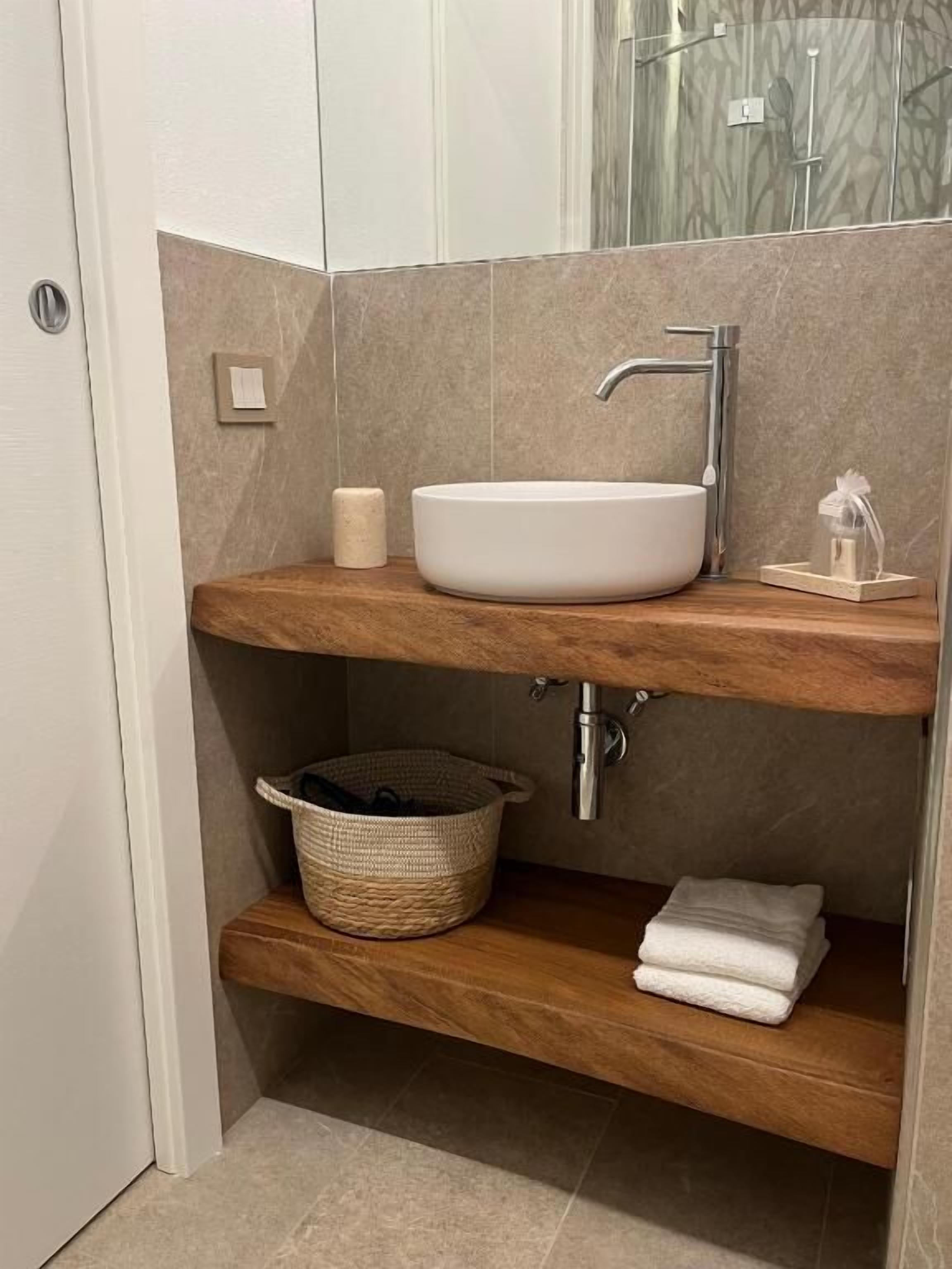 Un baño con lavamanos blanco, repisas de madera, una cesta y un perchero para toallas.