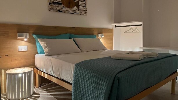 A neatly made bed with a wooden headboard, a bedside lamp, and a hanging light fixture. - Casetta in Calle (Chioggia)