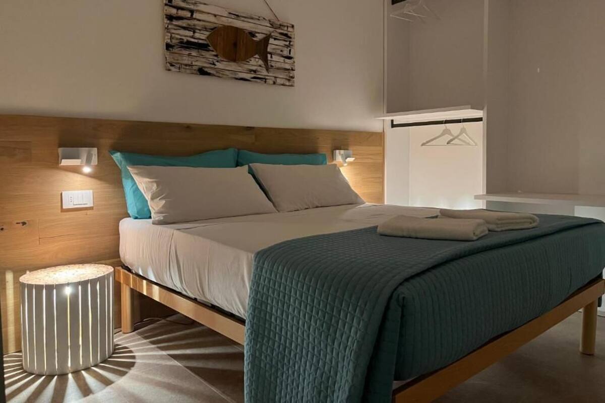 Una cama bien hecha con cabecera de madera, una lámpara de noche y una lámpara colgante.