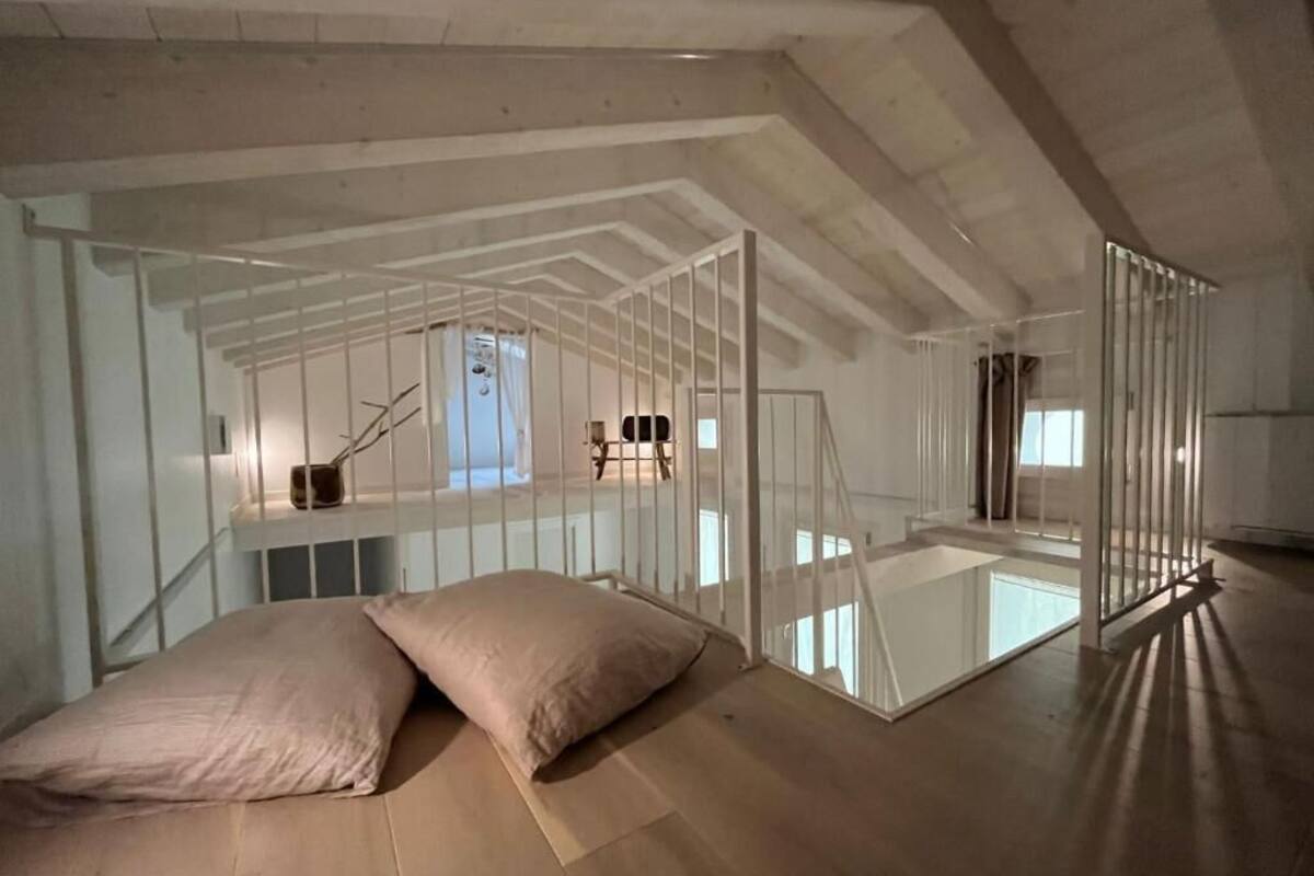 Una habitación con techos altos, un panel de vidrio, vigas de madera y una cama con almohadas.