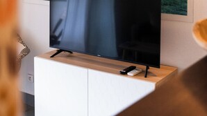 Un televisor de pantalla plana sobre un mueble blanco con tapa de madera, un control remoto y un cuadro colgado en la pared que muestra un muelle que se adentra en el agua.