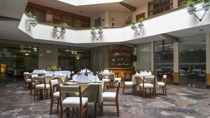 Un vestíbulo de hotel con varias mesas de comedor, sillas y una zona de bar central.