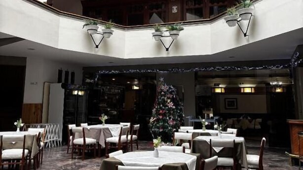 Un comedor con varios niveles, mesas y sillas, un árbol de Navidad y una escalera central.