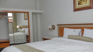 Habitación de hotel con cama, mesita de noche, espejo y lámpara de pared.